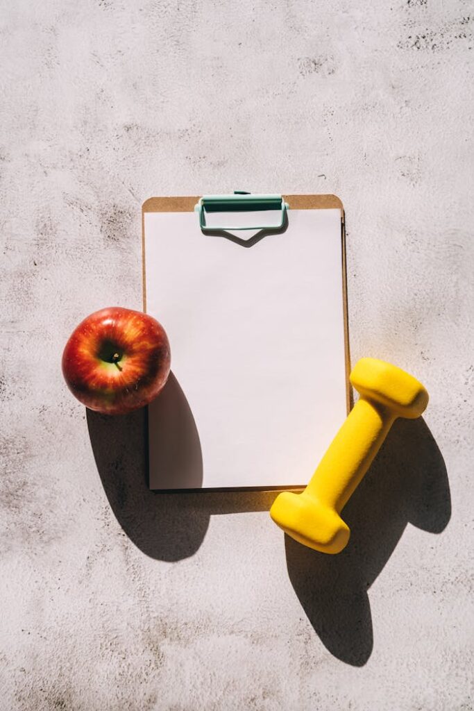 pexels-photo-8154260 Flat lay of apple, clipboard, and dumbbell representing fitness and nutrition concept.